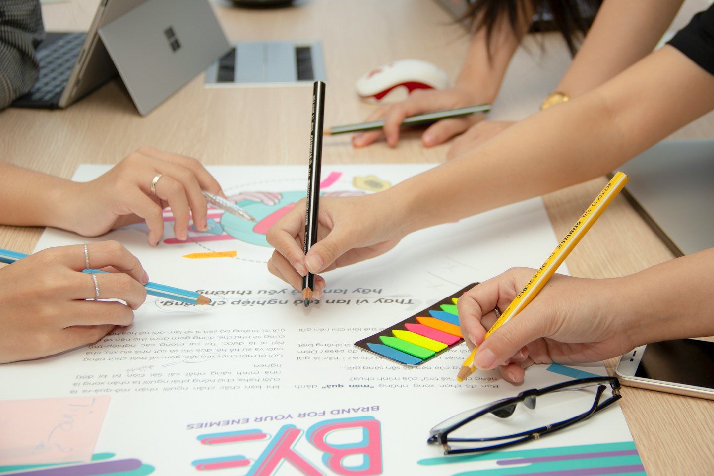 Hands collaborating on a design project with pencils and a laptop.