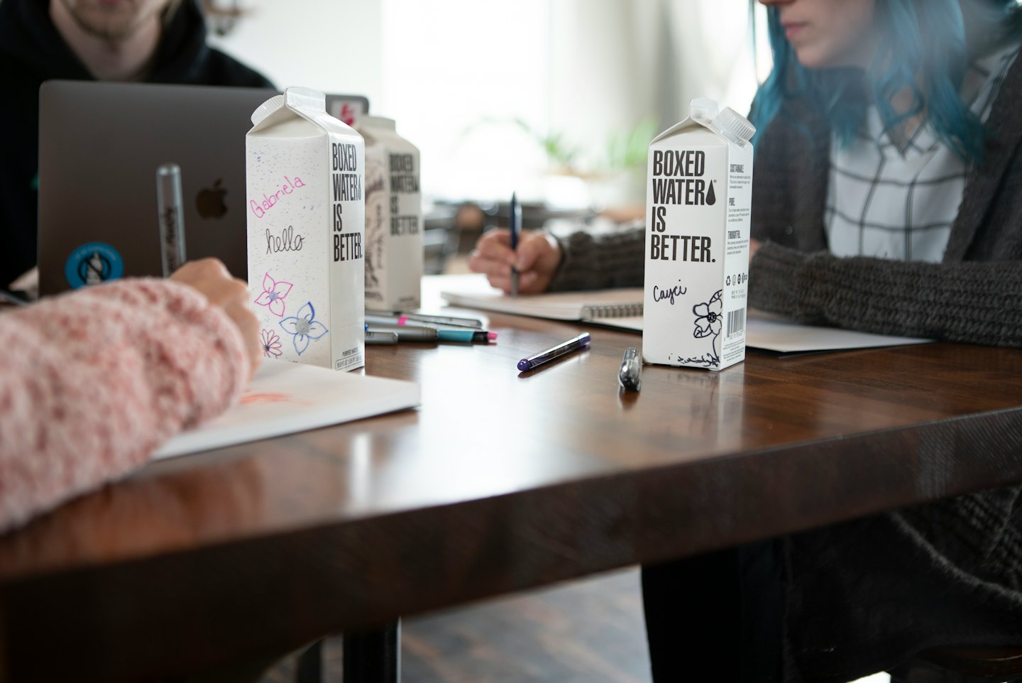 People collaborate around a table with laptops and boxed water.